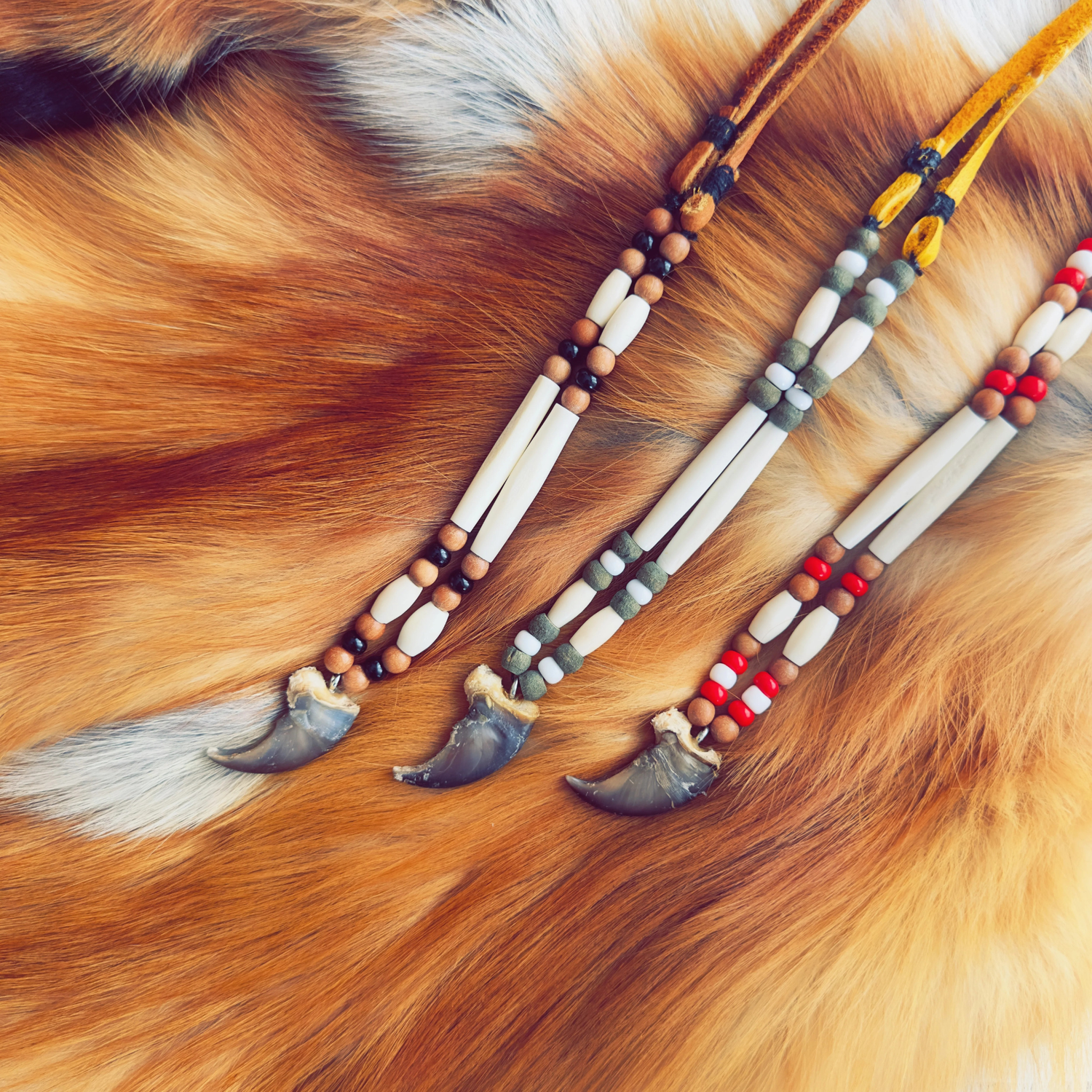 Handmade Indigenious bear claw necklaces displayed on natural fur, crafted with bone beads and moose hide cords.