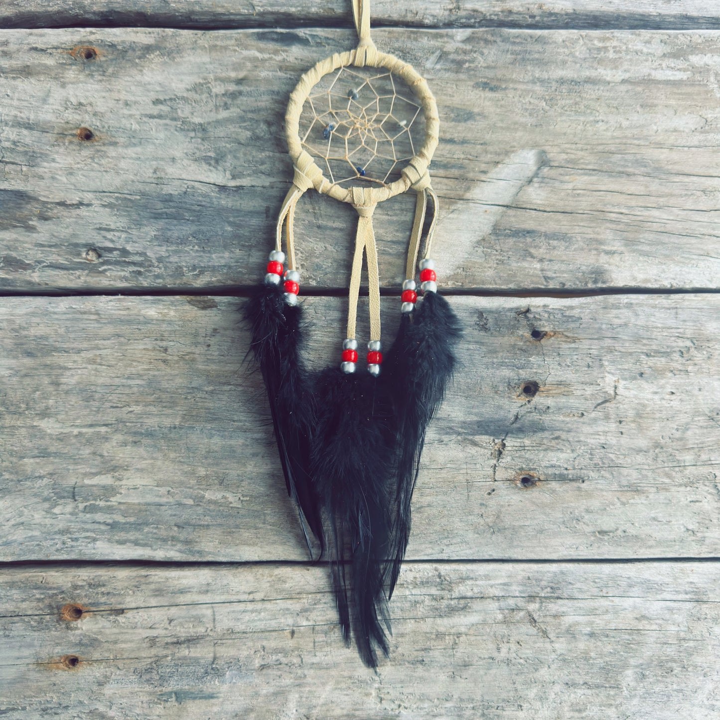 Artisanat autochtone : capteur de rêves de 3 pouces en cuir beige avec perles rouges et blanches, longues plumes noires élégantes sur fond de bois gris.