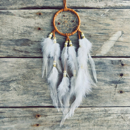 Artisanat autochtone : capteur de rêves de 3 pouces en cuir ocre jaune avec perles blanches et dorées, plumes blanches vaporeuses sur fond de bois de grange.