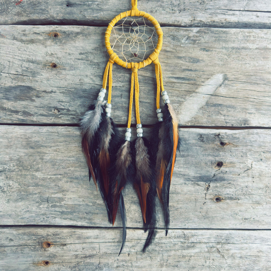 Artisanat autochtone : capteur de rêves de 3 pouces en cuir ocre jaune avec perles blanches et argentées, plumes naturelles brunes et orangées sur bois de grange.