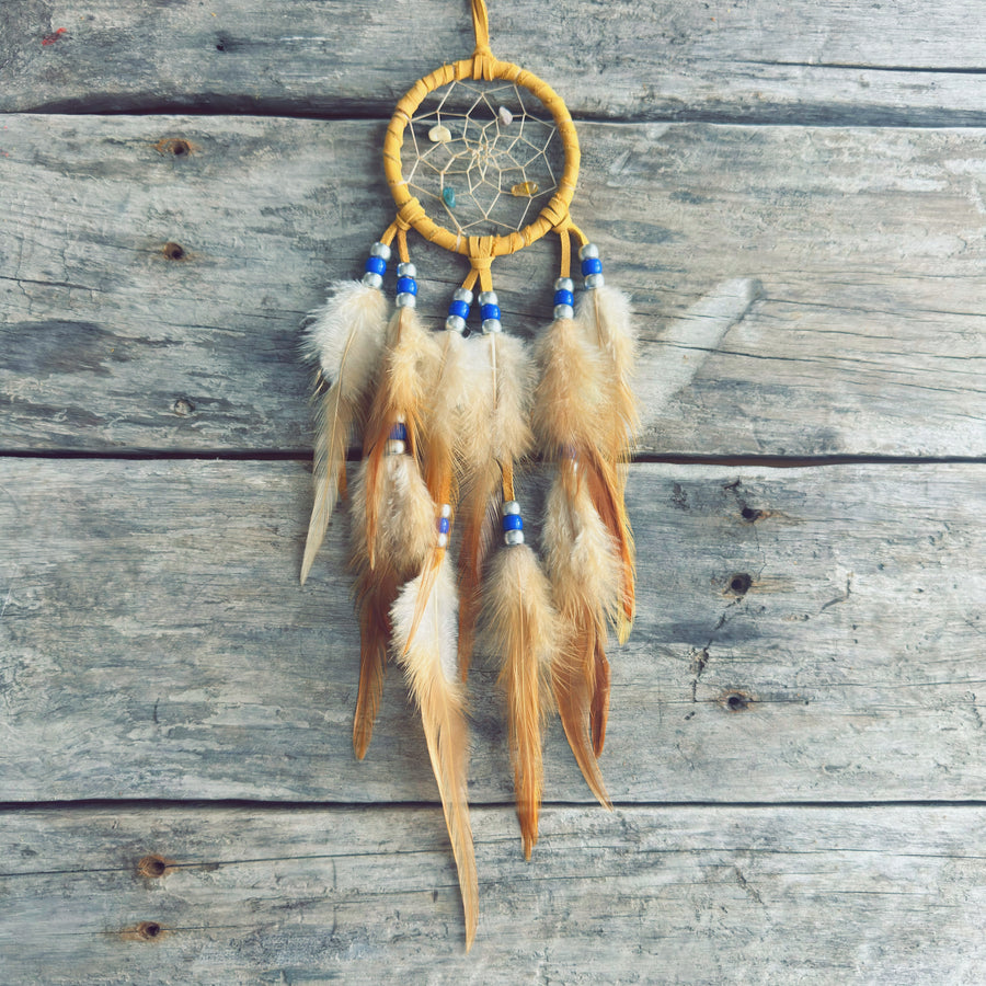 Artisanat autochtone : capteur de rêves de 3 pouces en cuir ocre jaune avec perles bleu royal et blanches, plumes naturelles beige crème sur fond de bois gris