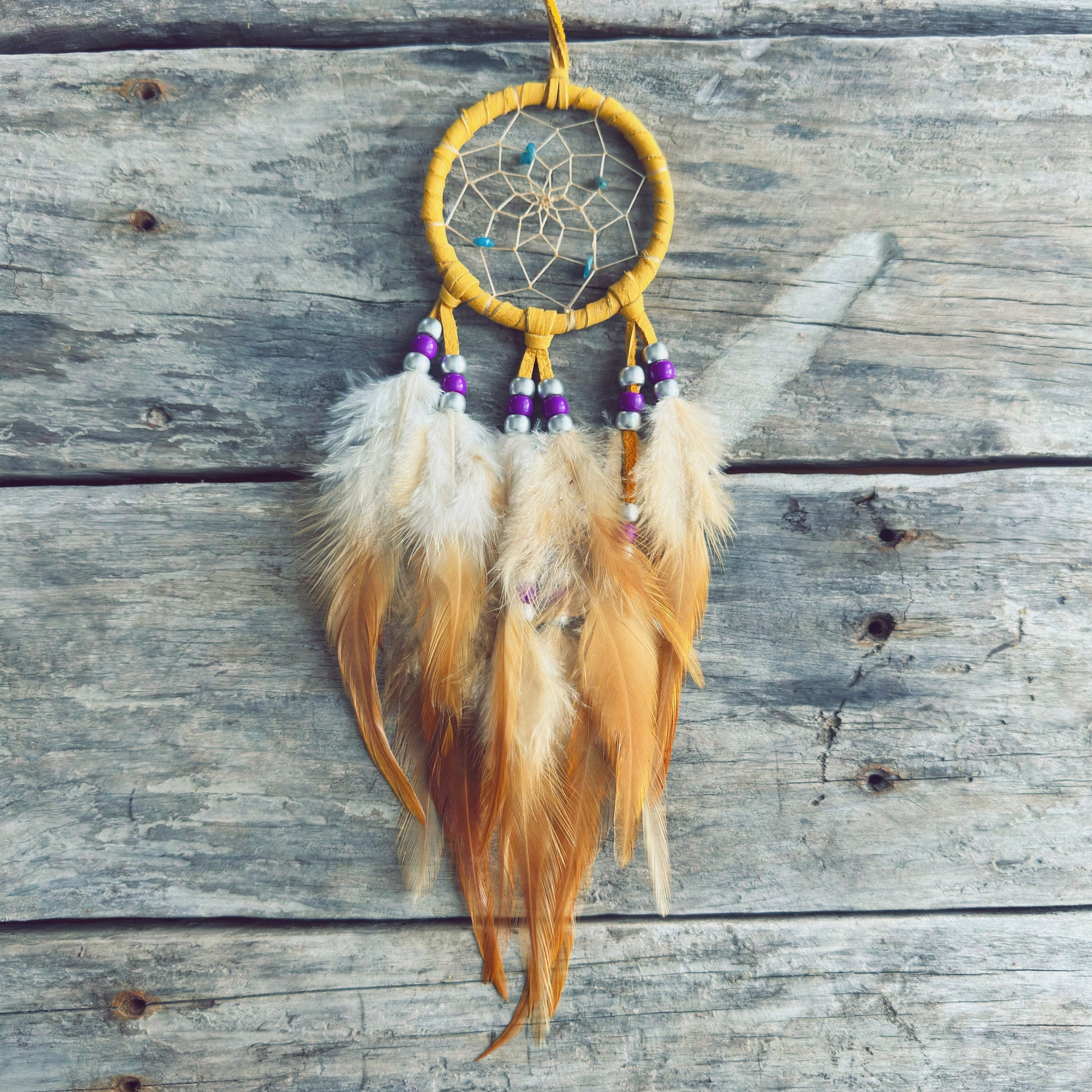 Artisanat autochtone : capteur de rêves de 3 pouces en cuir ocre jaune avec perles mauves, blanches et turquoises, plumes naturelles beige crème sur fond de bois