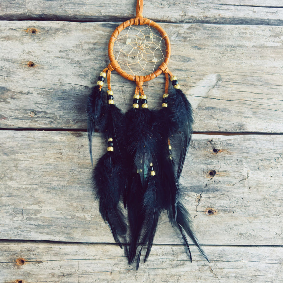 Artisanat autochtone : capteur de rêves de 3 pouces en cuir ocre jaune avec perles noires et dorées, longues plumes noires sur fond de bois de grange.