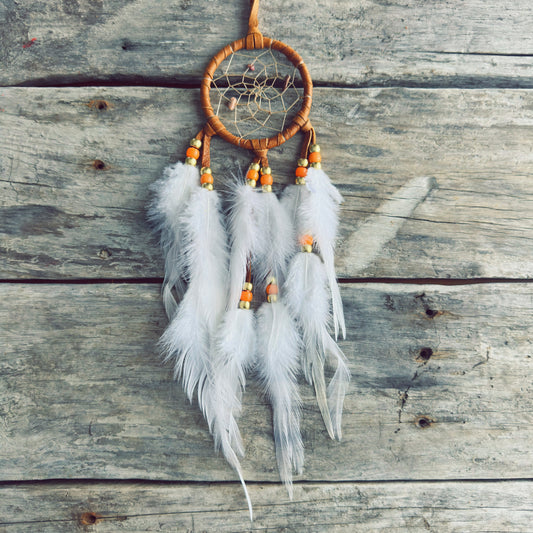 Artisanat autochtone : capteur de rêves de 3 pouces en cuir ocre jaune avec perles oranges et or, plumes blanches vaporeuses sur fond de bois gris.