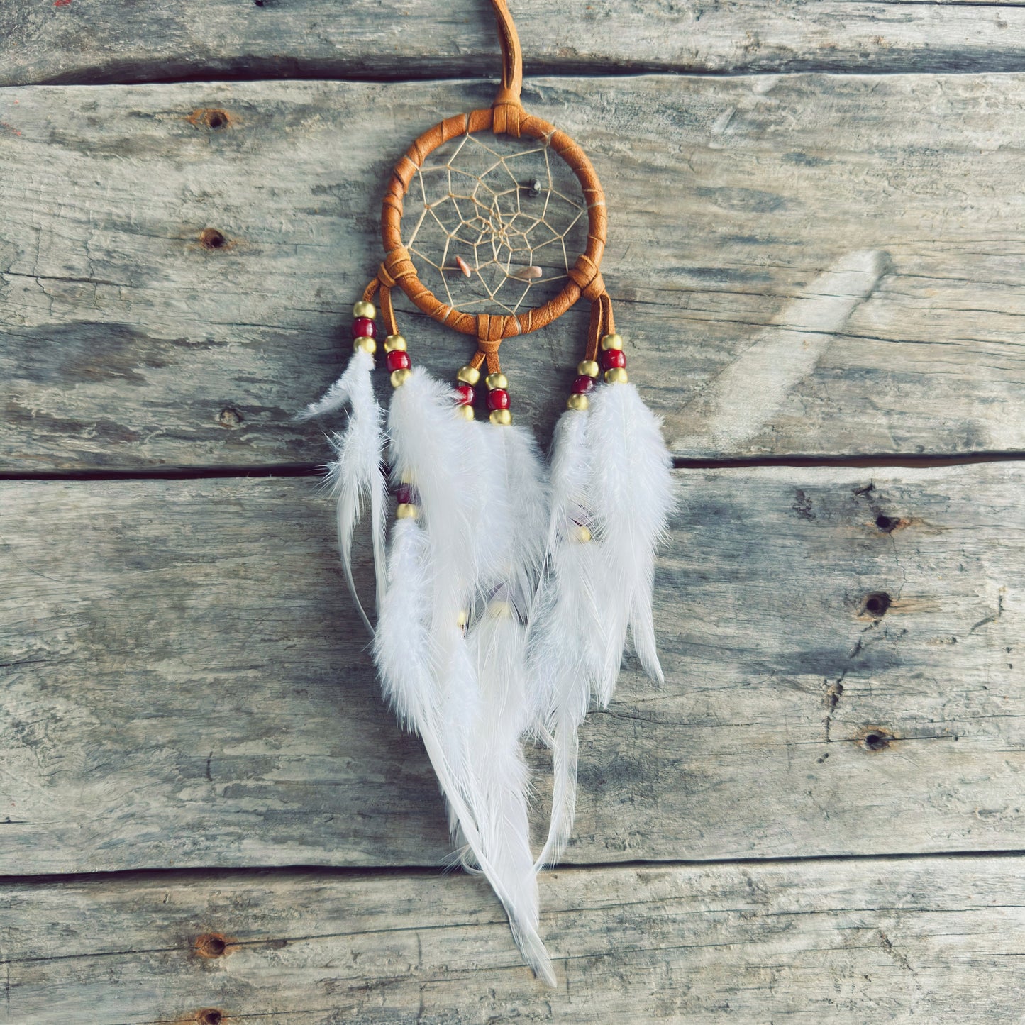 Artisanat autochtone : capteur de rêves de 3 pouces en cuir ocre jaune avec perles rouges et dorées, plumes blanches vaporeuses sur fond de bois gris.