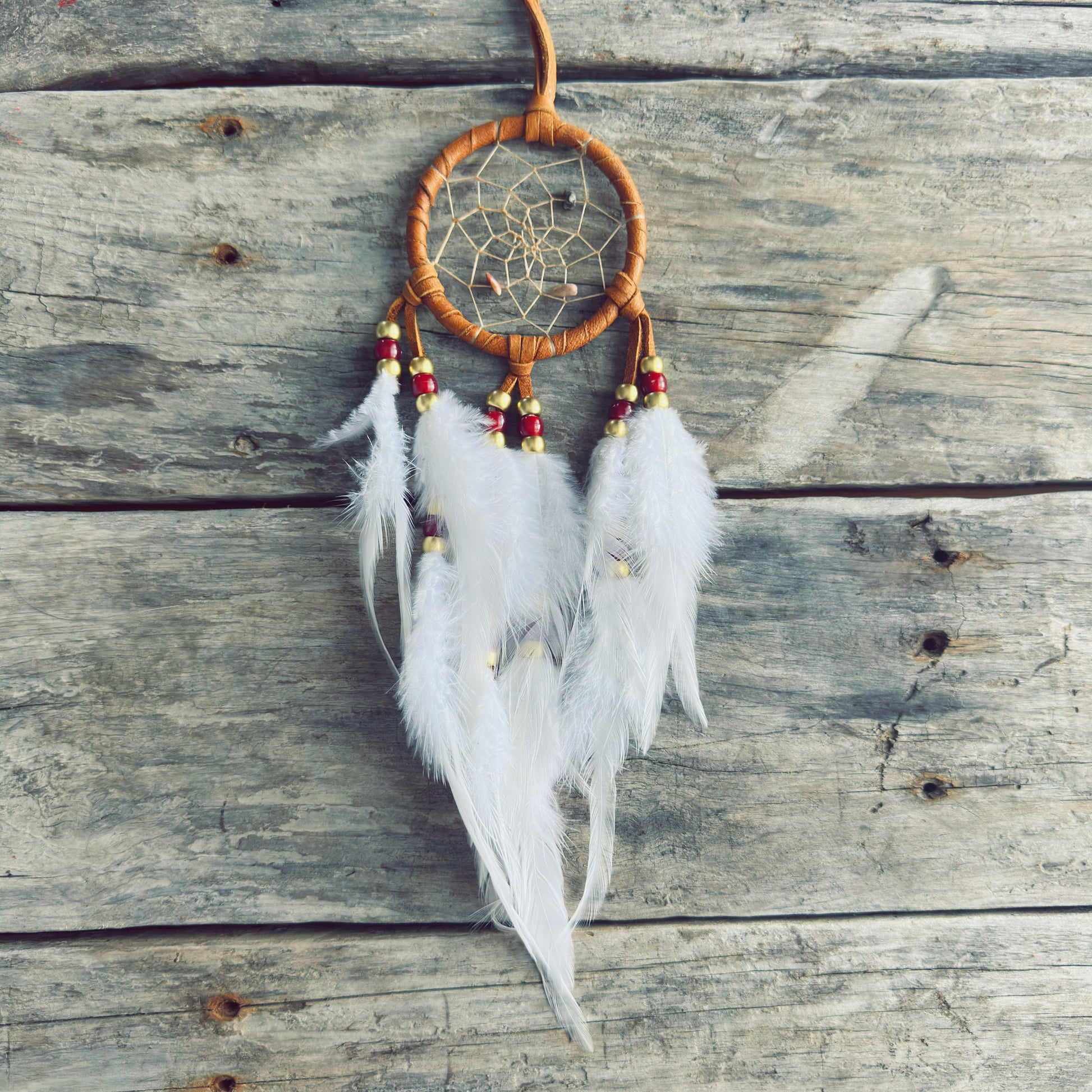 Artisanat autochtone : capteur de rêves de 3 pouces en cuir ocre jaune avec perles rouges et dorées, plumes blanches vaporeuses sur fond de bois gris.