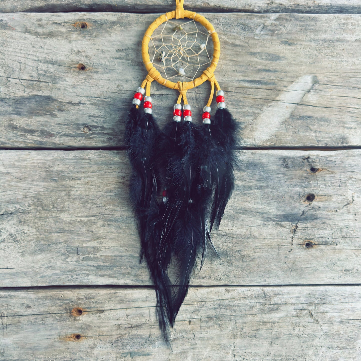 Artisanat autochtone : capteur de rêves de 3 pouces en cuir ocre jaune avec perles rouges et blanches, longues plumes noires sur fond de bois gris rustique