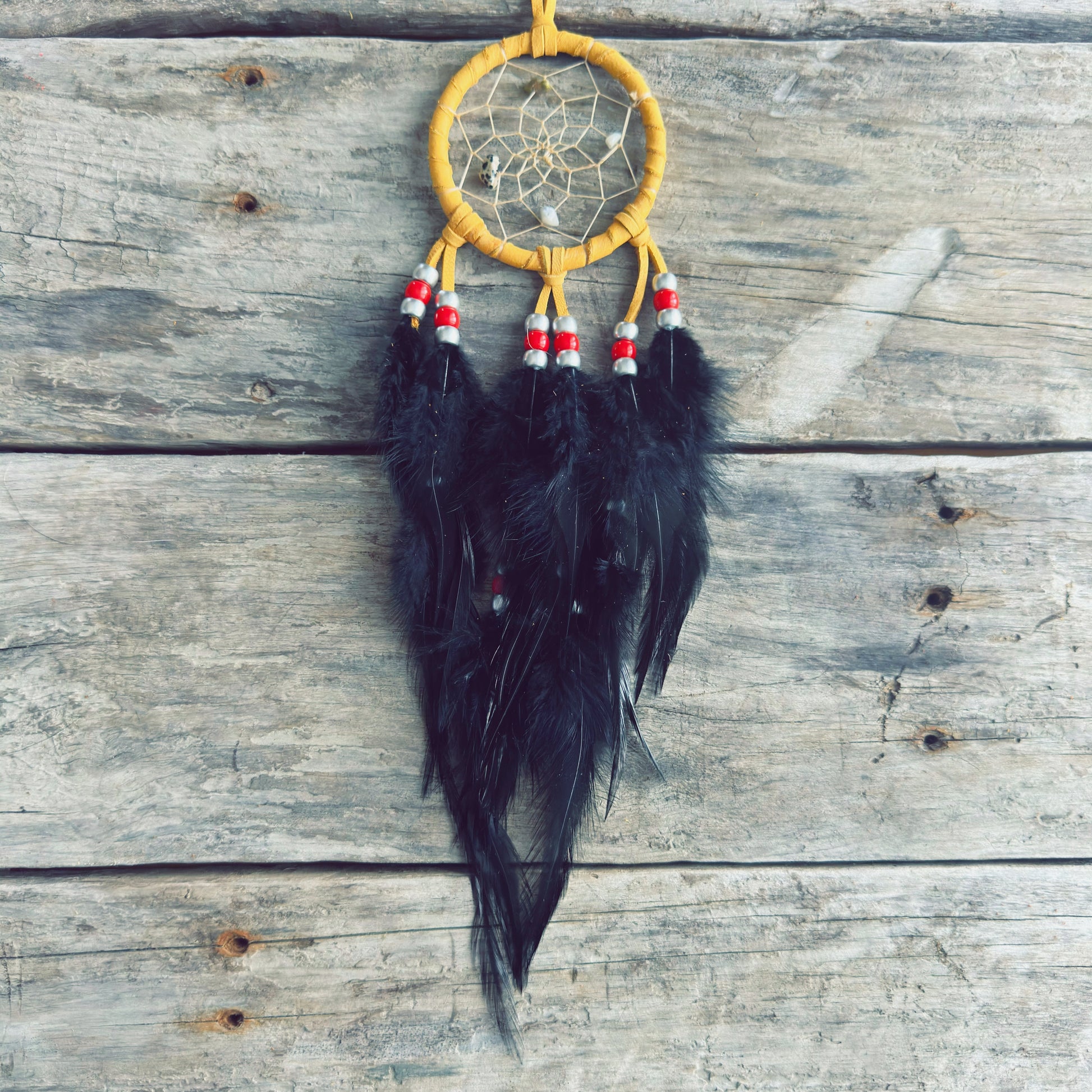 Artisanat autochtone : capteur de rêves de 3 pouces en cuir ocre jaune avec perles rouges et blanches, longues plumes noires sur fond de bois gris rustique