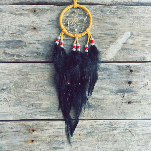 Artisanat autochtone : capteur de rêves de 3 pouces en cuir ocre jaune avec perles rouges et blanches, longues plumes noires sur fond de bois gris rustique