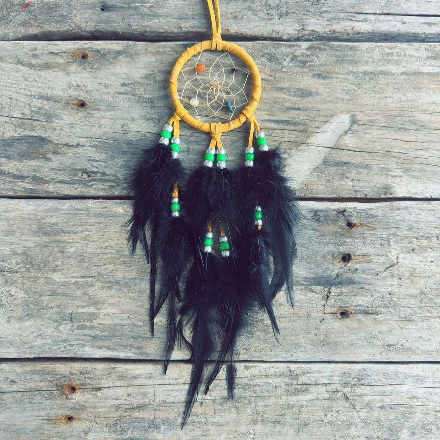 Artisanat autochtone : capteur de rêves de 3 pouces en cuir ocre jaune avec perles vert lime et blanches, longues plumes noires sur fond de bois de grange