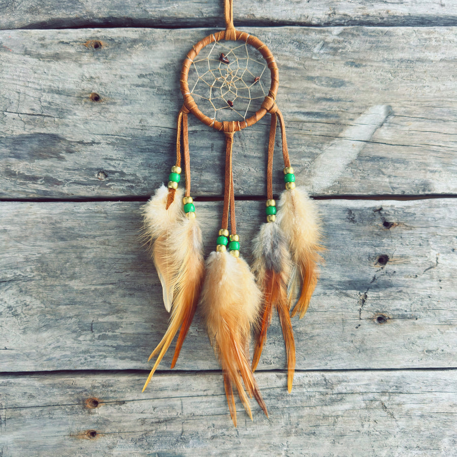 Artisanat autochtone : capteur de rêves de 3 pouces en cuir ocre jaune avec perles vert lime et or, plumes naturelles beige et orangées sur fond de bois gris