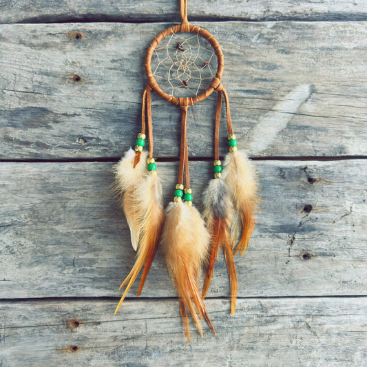 Artisanat autochtone : capteur de rêves de 3 pouces en cuir ocre jaune avec perles vert lime et or, plumes naturelles beige et orangées sur fond de bois gris