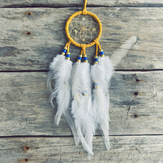 Artisanat autochtone : capteur de rêves de 3 pouces en cuir ocre jaune avec perles bleu royal et or, plumes blanches vaporeuses sur fond de bois vieilli.