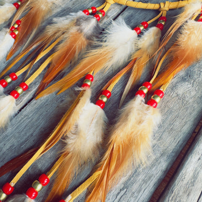 Gros plan sur les perles rouges et dorées et les plumes de coq.