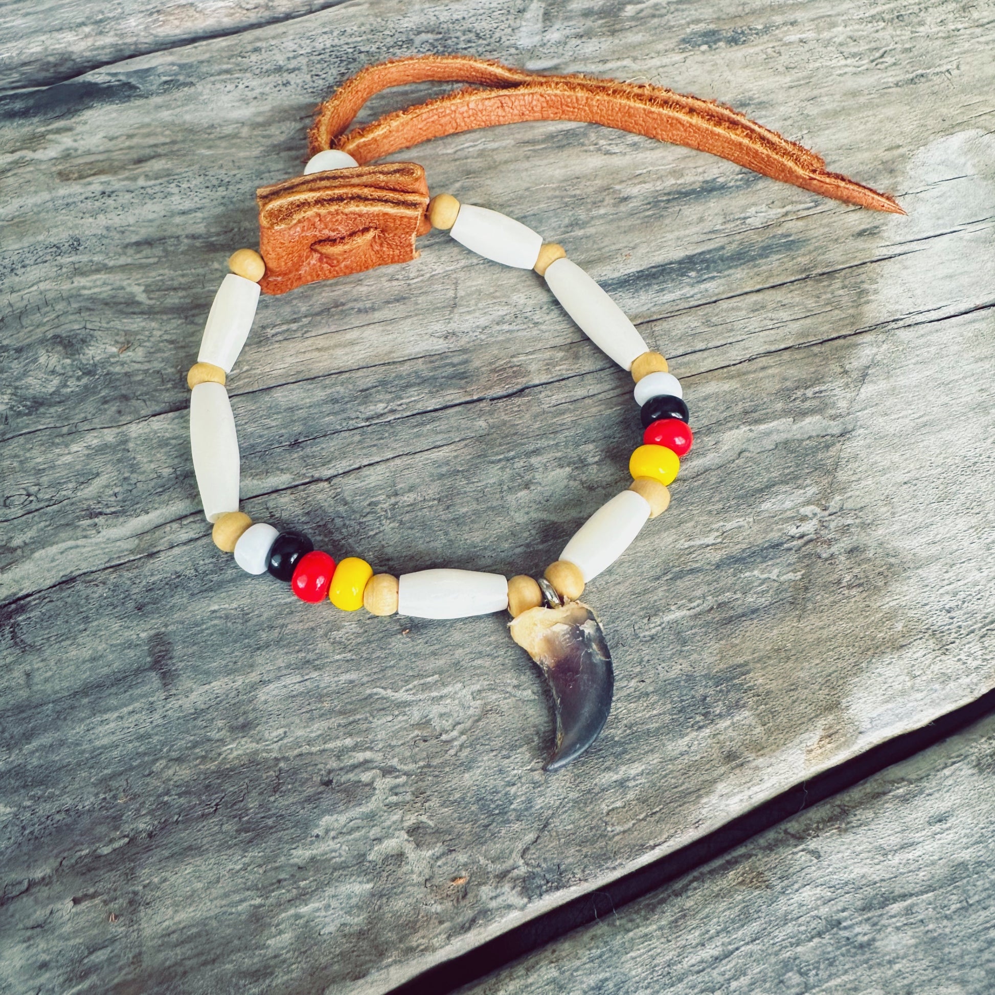 Vue détaillée du bracelet autochtone avec véritable griffe de loup, mettant en valeur les perles d'os, les perles de verre et le cuir d'orignal fabriqués à la main par un artisan Ilnu.