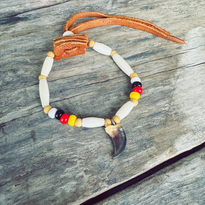 Vue détaillée du bracelet autochtone avec véritable griffe de loup, mettant en valeur les perles d'os, les perles de verre et le cuir d'orignal fabriqués à la main par un artisan Ilnu.
