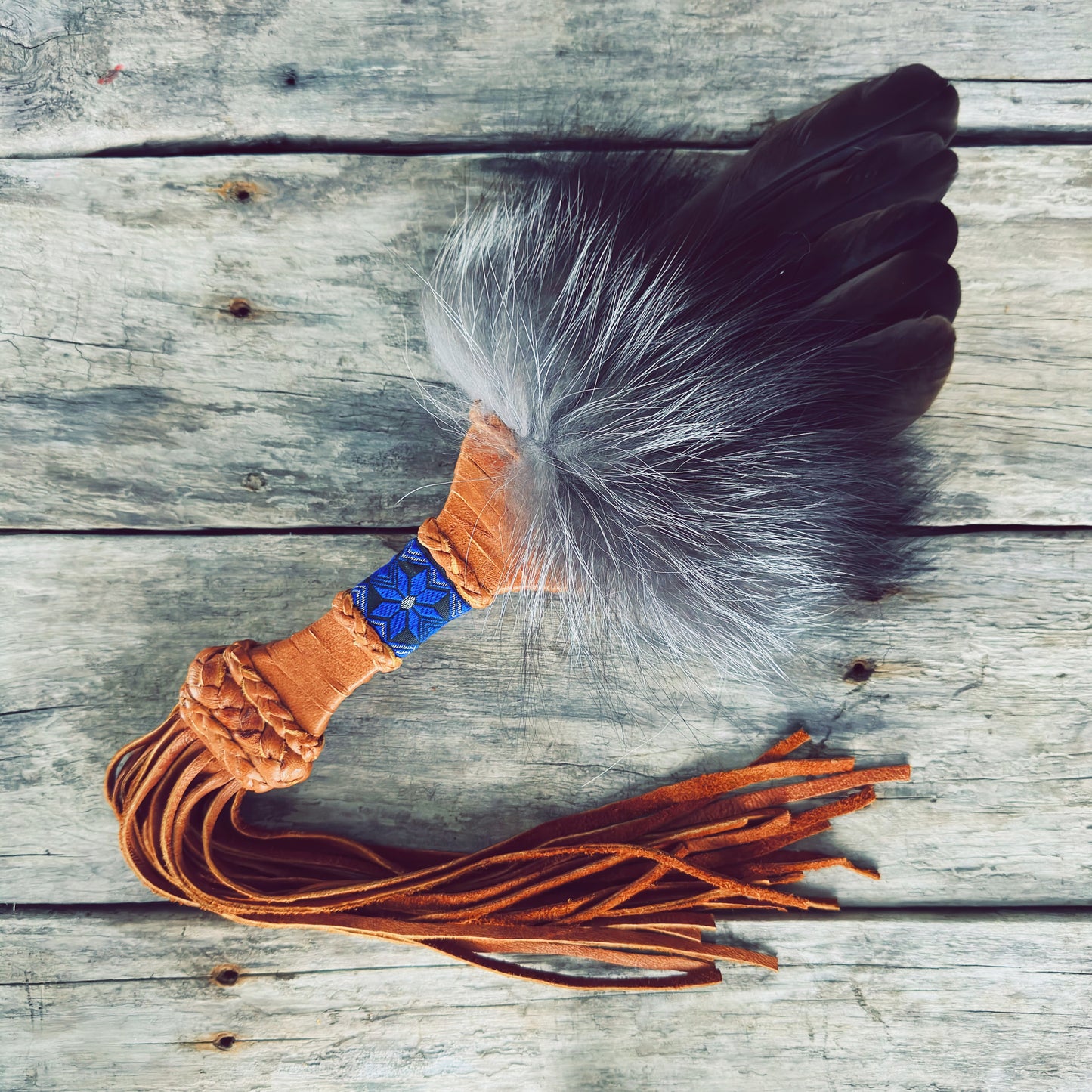 Éventail de purification autochtone artisanal en fourrure et plumes naturelles avec poignée en cuir tressé et perles bleues.