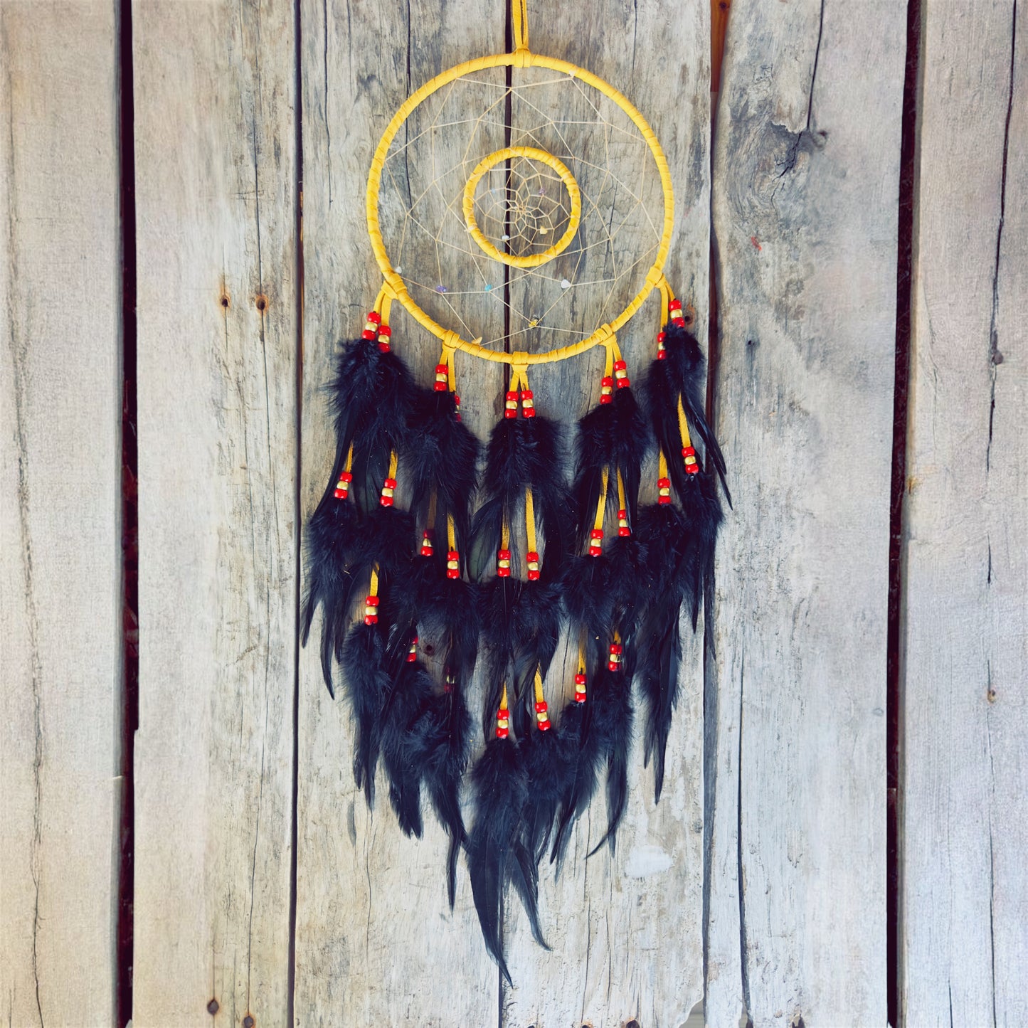 Artisanat autochtone : grand capteur de rêves de 8 pouces en cuir ocre jaune avec double cerceau, perles rouges et or, longues plumes noires sur fond de bois.