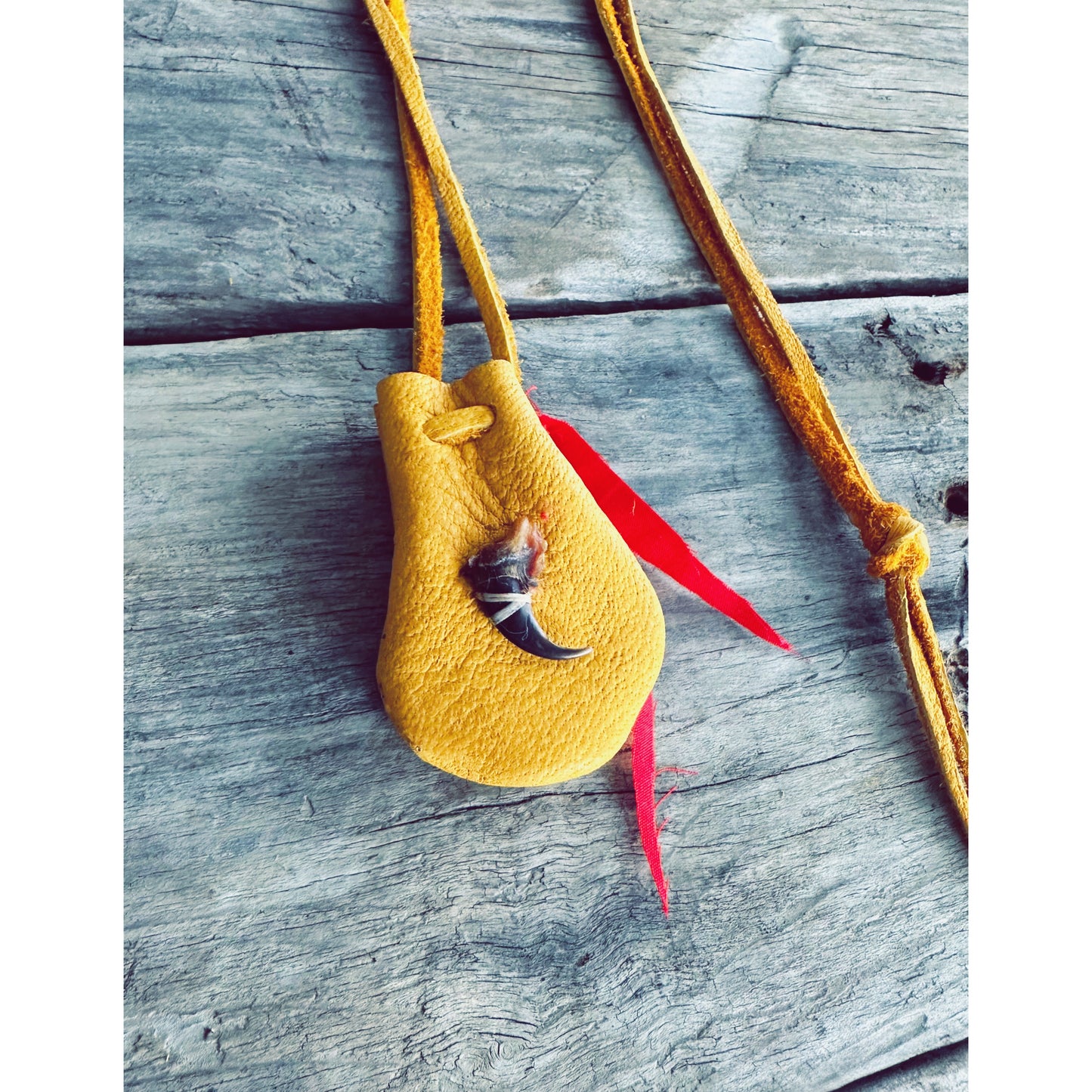 sac de medecine autochtone en cuir d’orignal avec veritable griffe de loup et ruban rouge sur fond de bois
